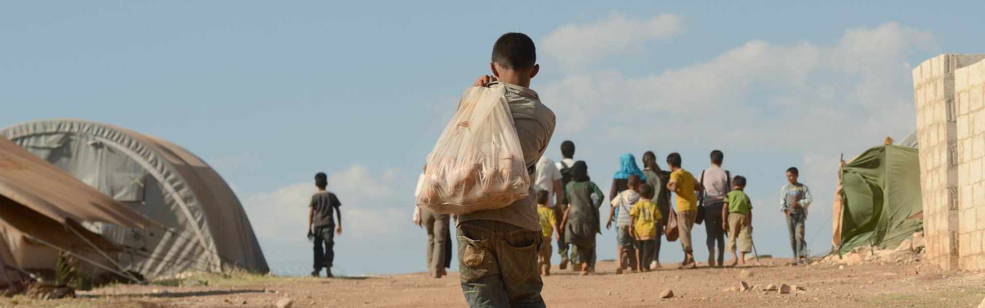 Child carrying a bag of belongings in a desert environment