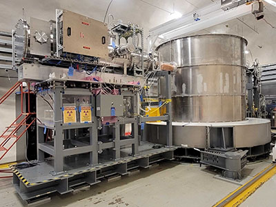 Large industrial scientific apparatus with a cylindrical metal tank and radiation warning symbols on the control equipment